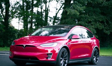 TESLA RED CAR PARKED ON ASPHALT ROAD 