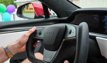 MAN HOLDING A YOKE SHAPED STEERING WHEEL OF A TESLA ELECTRIC CAR