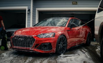 A RED CAR BEING WASHED BY A GARAGE 