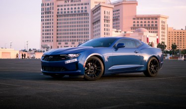 BLUE CHEVROLET SPORTS CAR PARKED ON THE ROAD NEAR CITY BUILDINGS